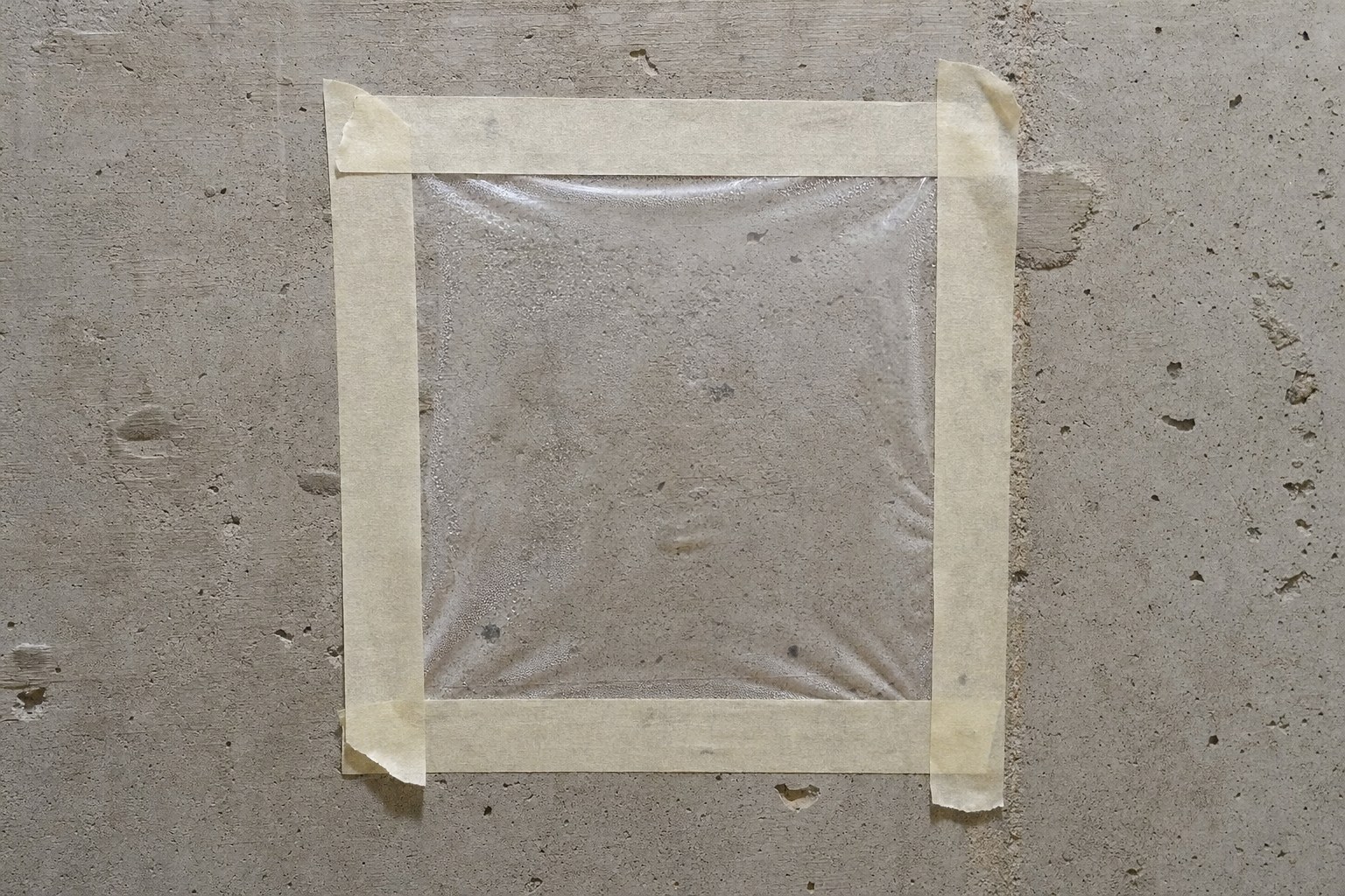 Clear plastic square taped to a concrete basement wall for a moisture test